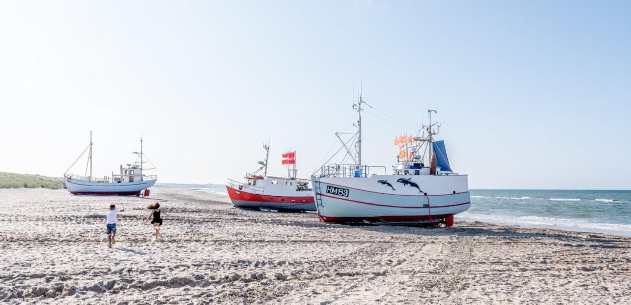 Barn som løper på stranden ved fiskebåter i Danmark