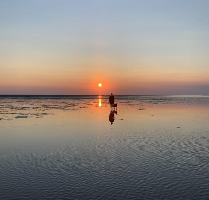 A woman walking her dog on the banks in the Wadden Sea National Park.
